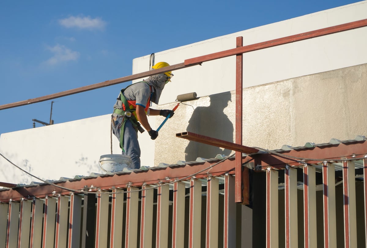 builder worker painting facade of high-rise building with roller