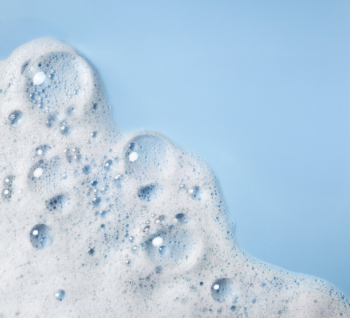 White soap foam with bubbles on a blue background, texture of the soapy or detergent foam
