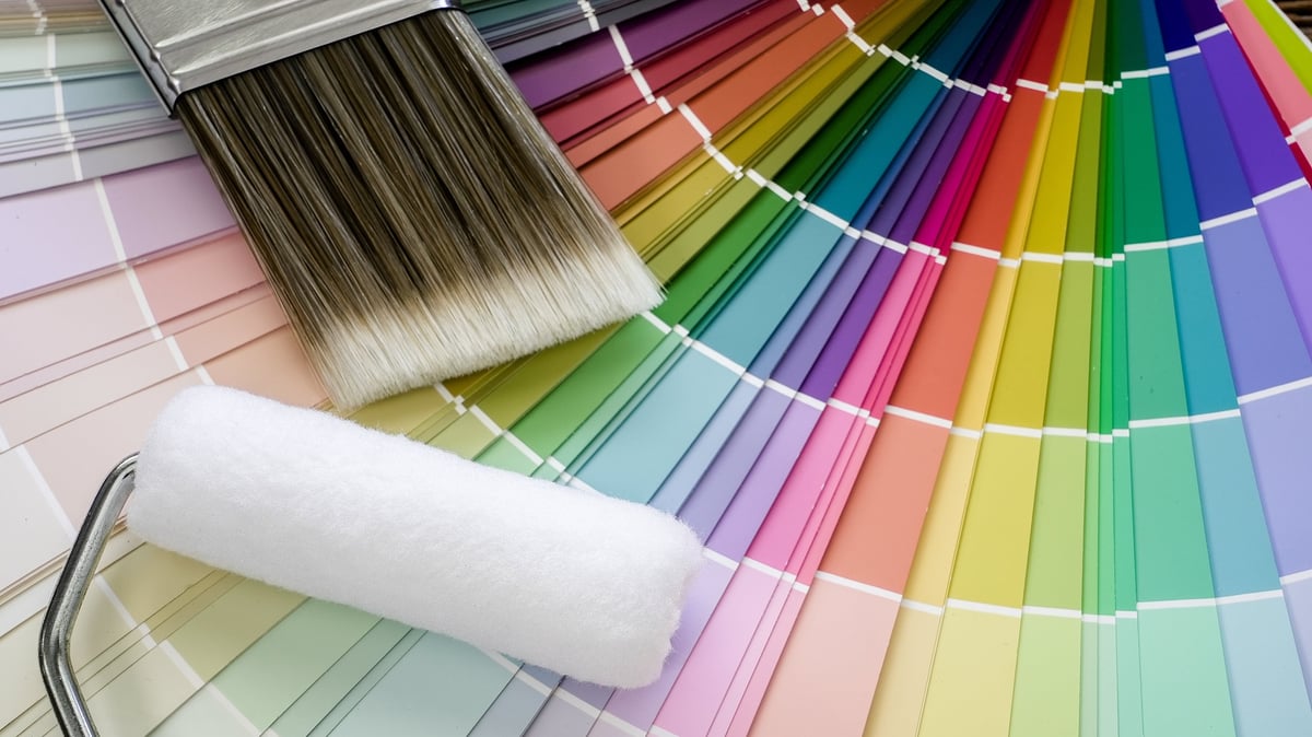 Paint tools resting on a fan of rainbow color swatches, representing home renovation, interior design, and decorating choices